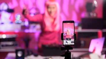 Woman with pink hair playing techno song at professional turntables while filming music process with phone camera, having fun in studio. Dj artist doing performance at nightclub with audio equipment